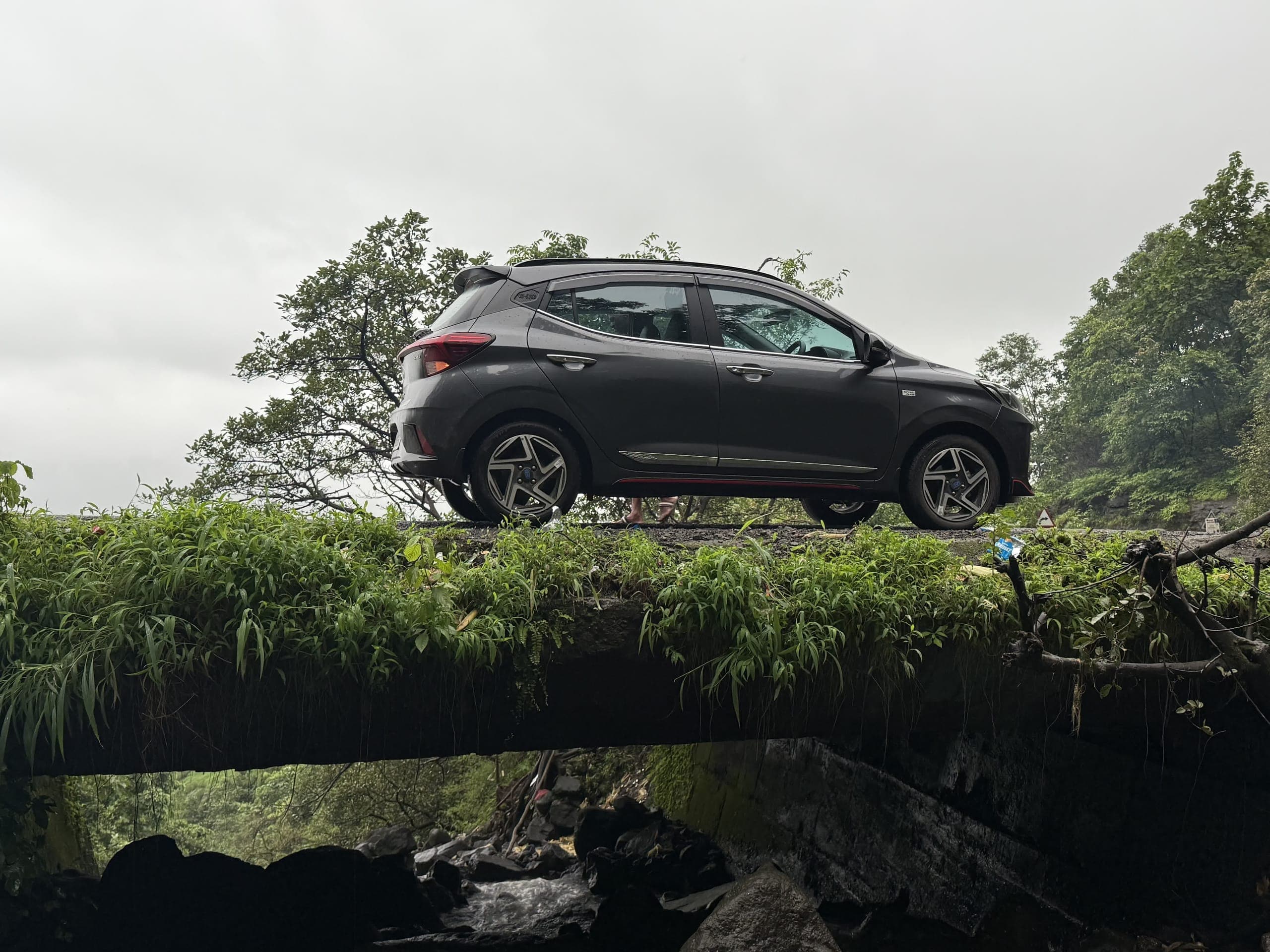 The car parked side-on on a mossy stone bridge over a monsoon stream