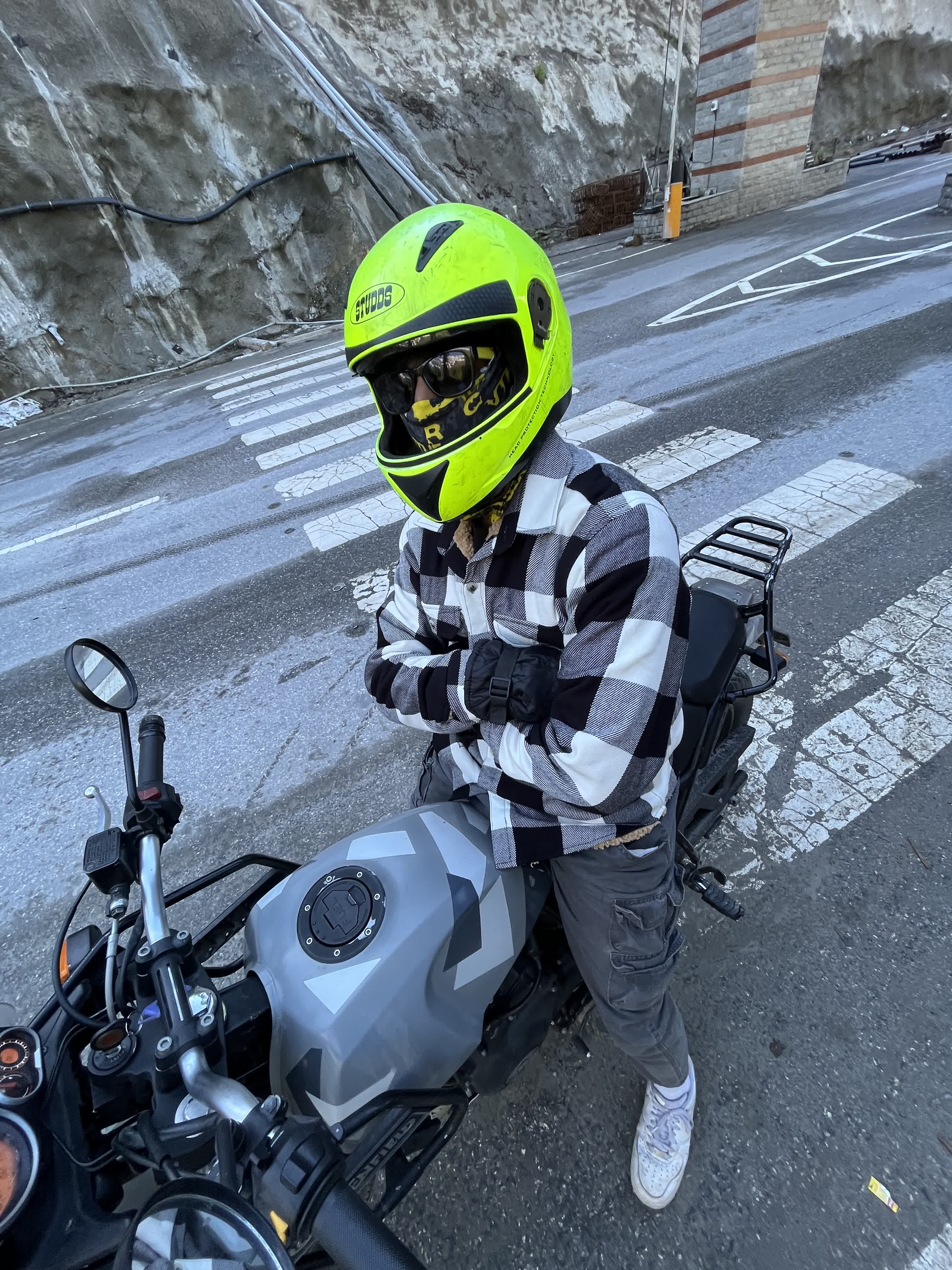 In a checked flannel and neon helmet beside the motorbike on a wet road
