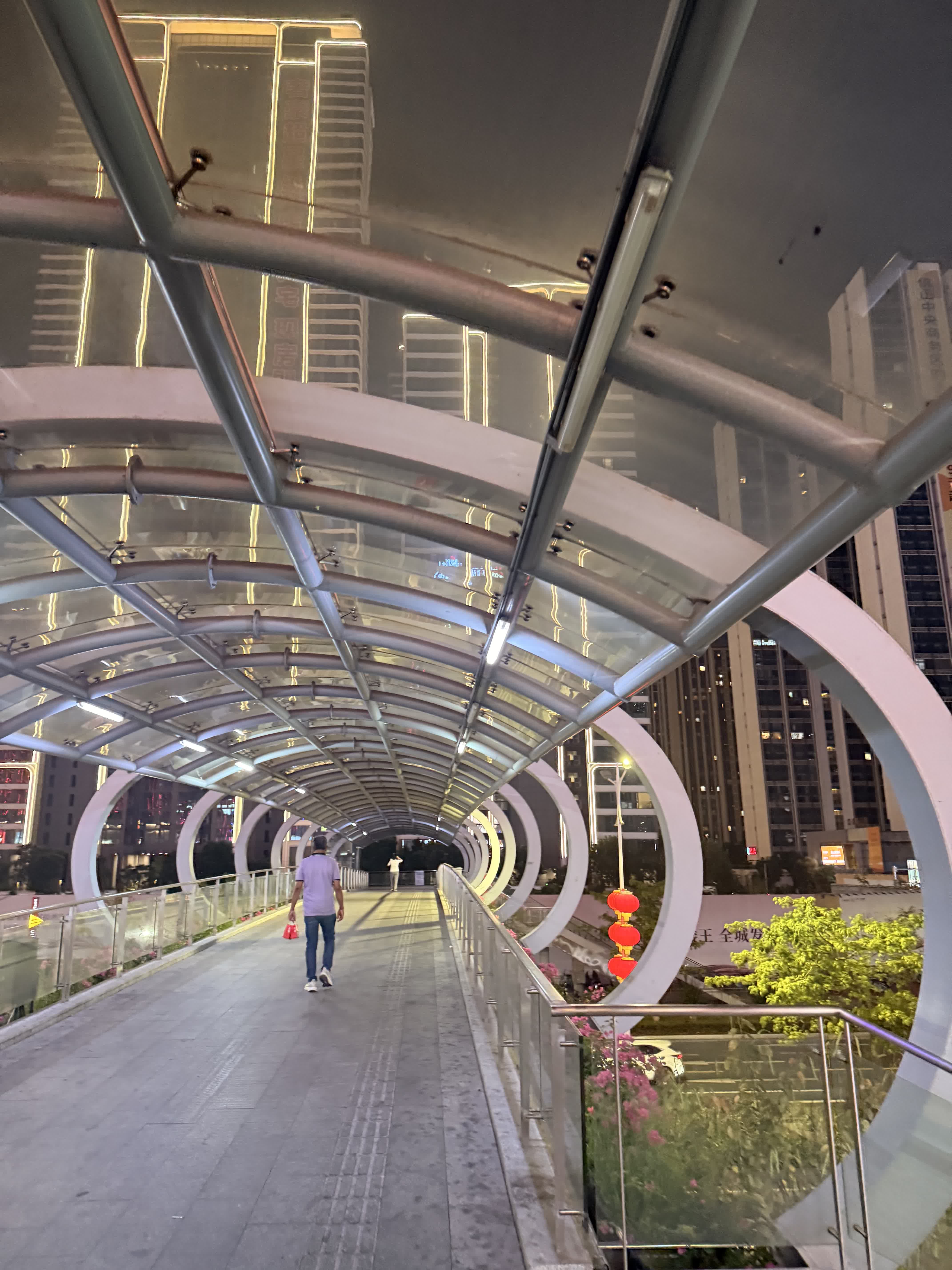 A curved glass pedestrian skywalk lit up at night between towers