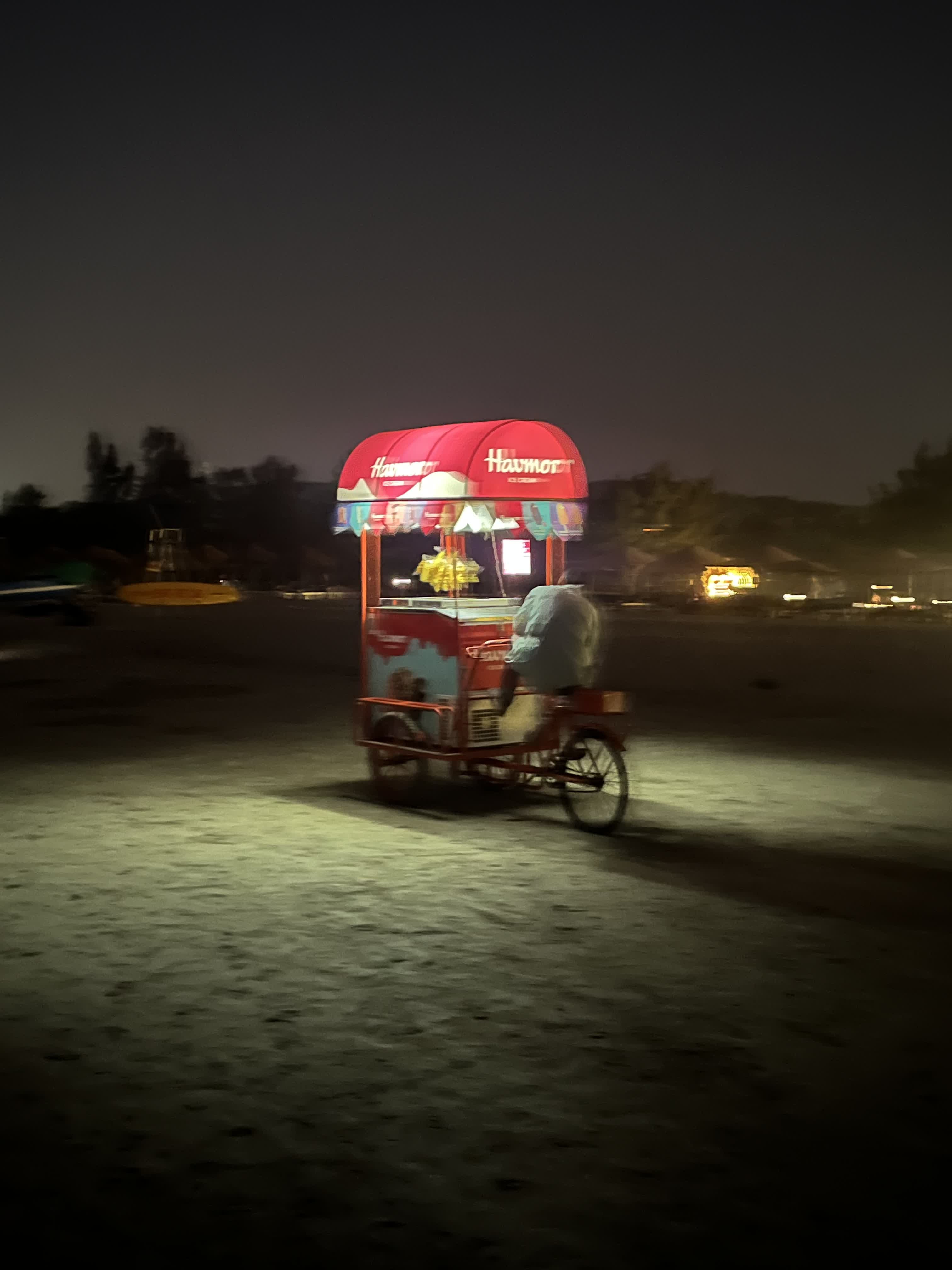 A lit Havmor ice-cream cart on the dark beach at night
