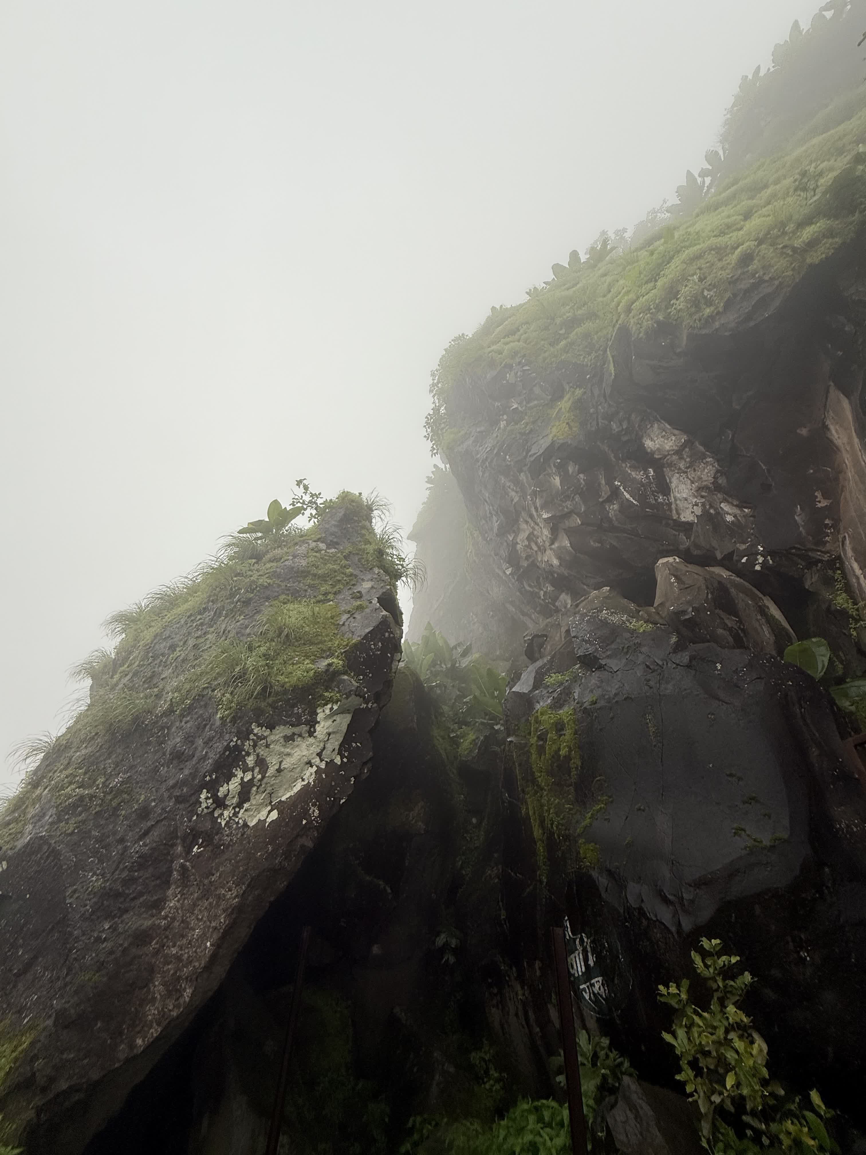 Mist-shrouded rock cliffs of Sinhagad, green with monsoon moss