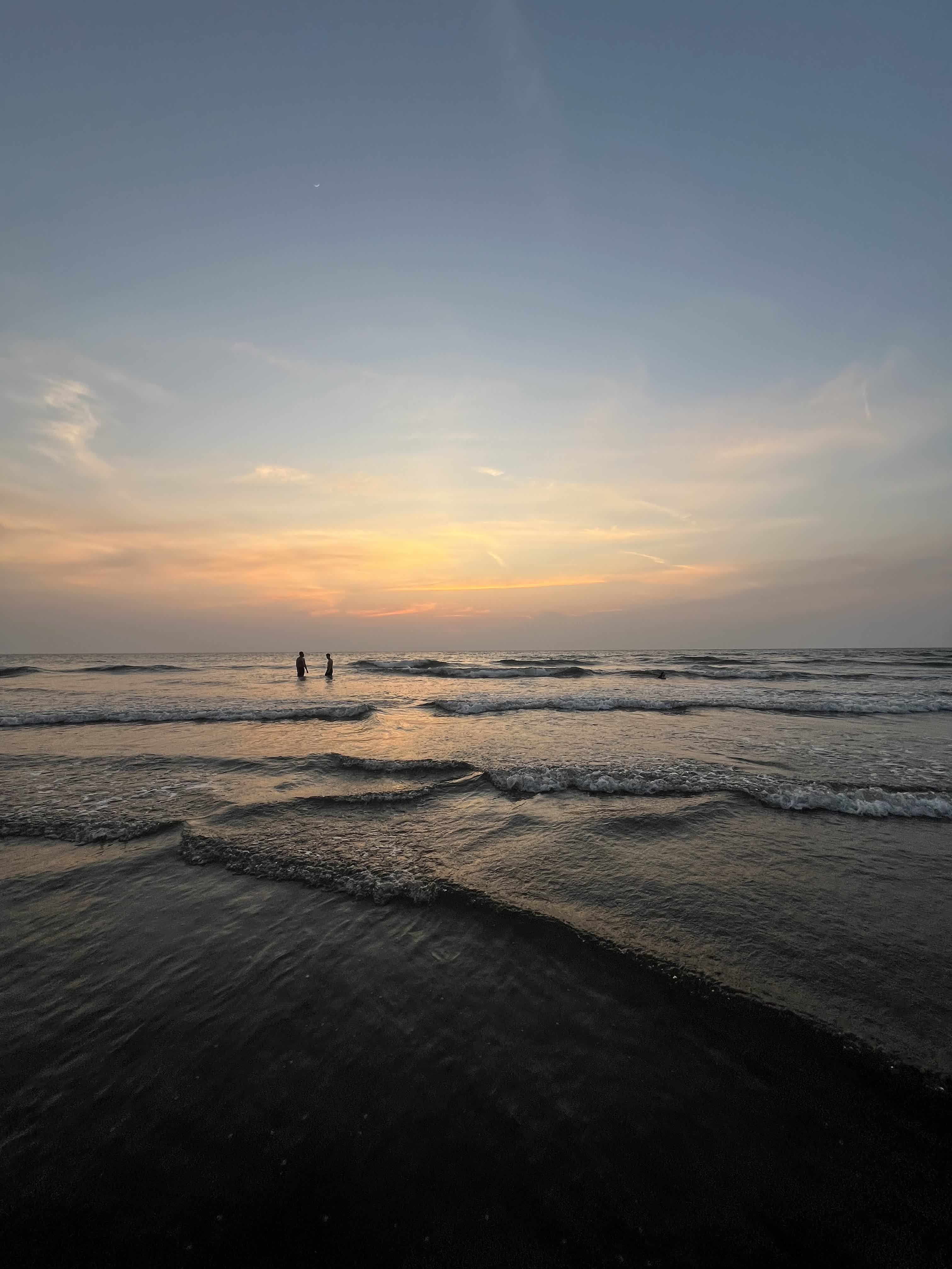 Two silhouettes wading into the sea at sunset
