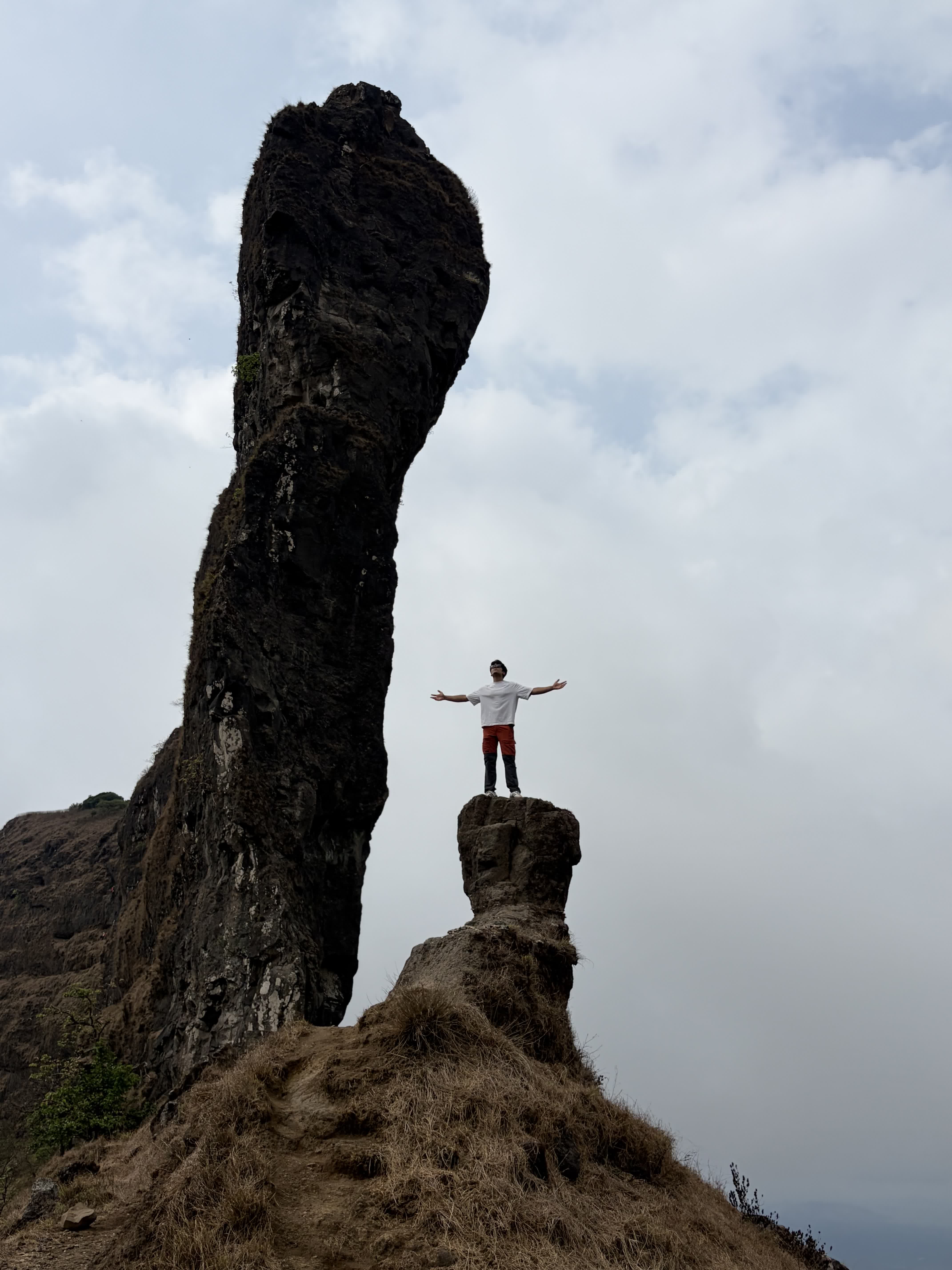 Standing arms wide on a rock spur beside the towering Tail Baila pinnacle