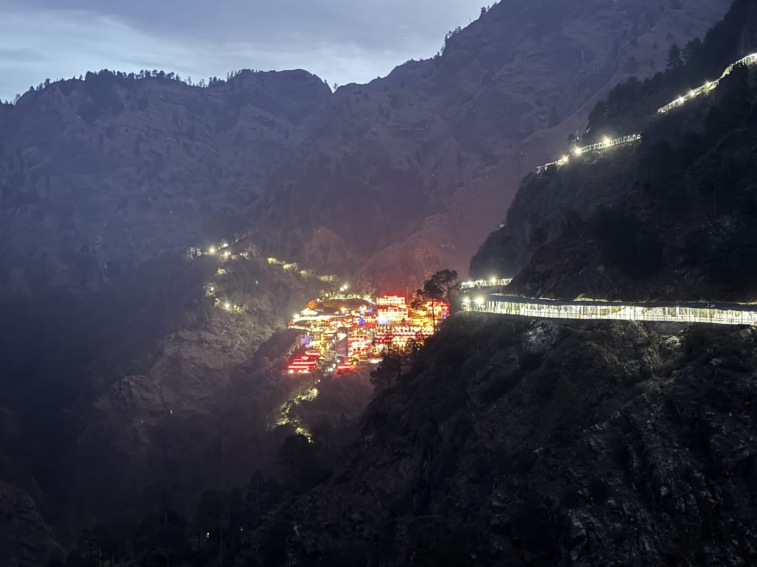 The Vaishno Devi shrine lit up red and gold on the mountainside at night